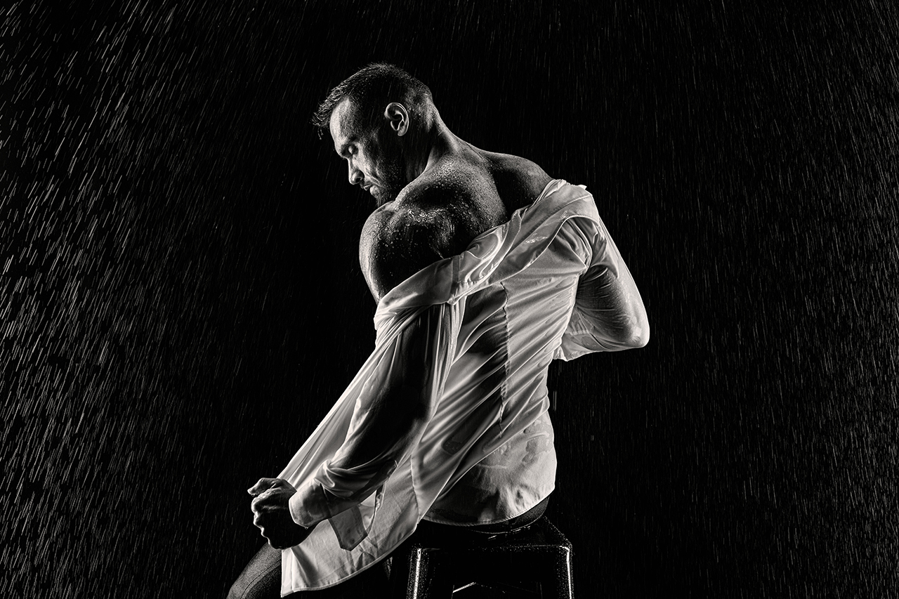 férfi boudoir fotózás, Férfi ül a széken háttal és esik az eső és félig letolja a vizes ingjét