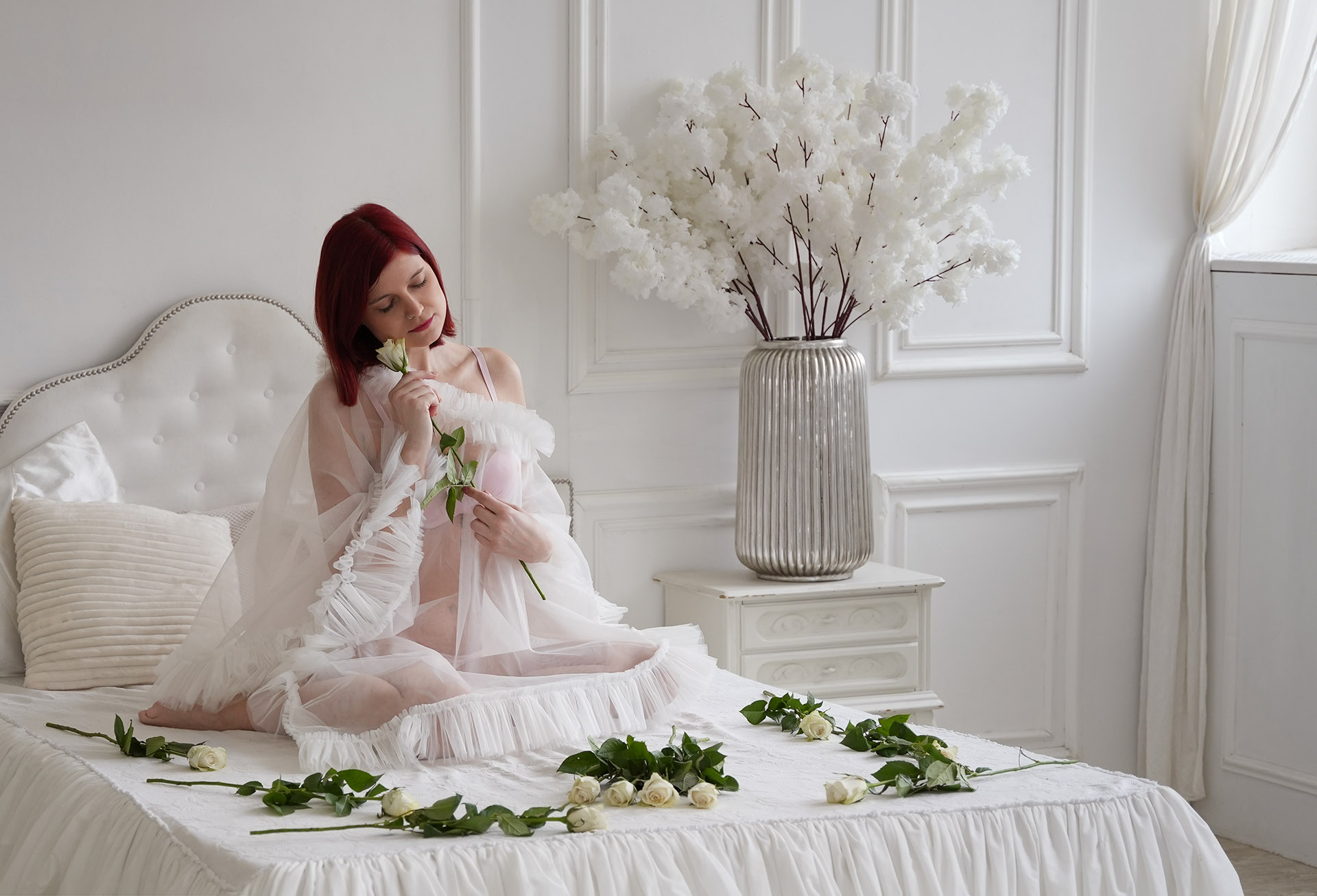 Pózolási segítség, Fiatal nő ül az ágyon egy fehér rózsát tart az arcához
