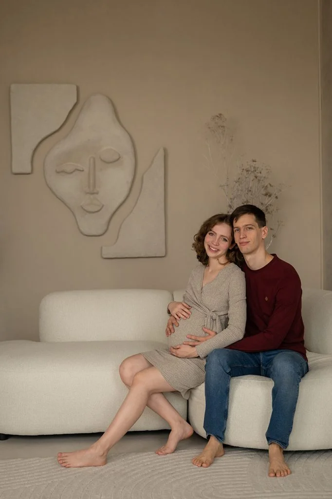 Pár kanapén ülve, egymást átölelve, kismama pocakját simogatva.