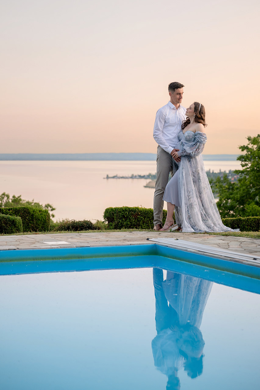 Várandós pár naplementében a Balaton panorámájával és medencével az előtérben.
