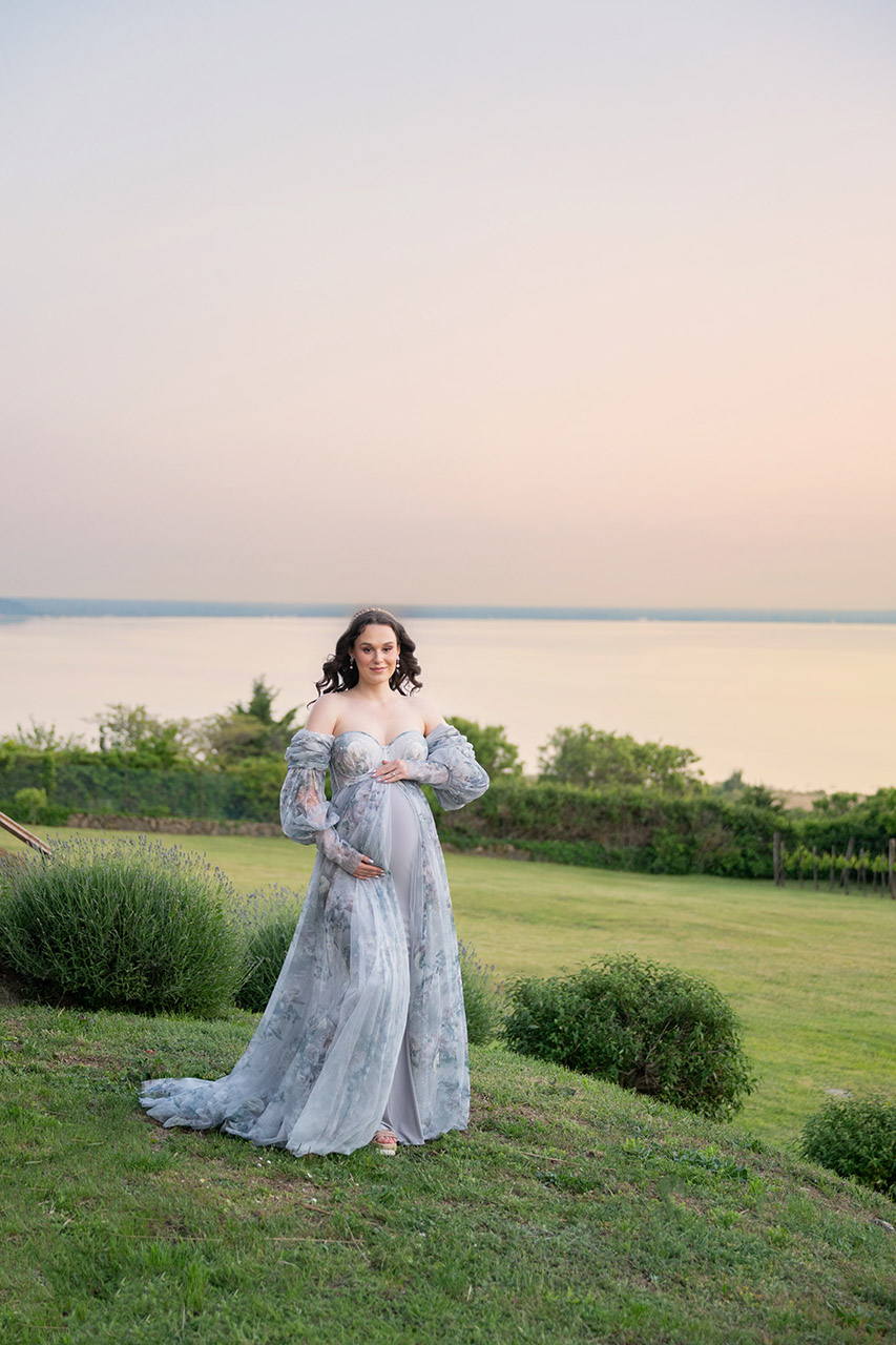 Kismama világoskék ruhában a Balaton partjára néző panorámával naplementekor, háttérben a Balaton.